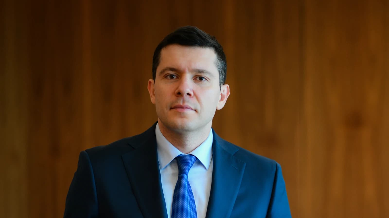 Антон Алиханов в синем костюме стоит у кресла в кабинете