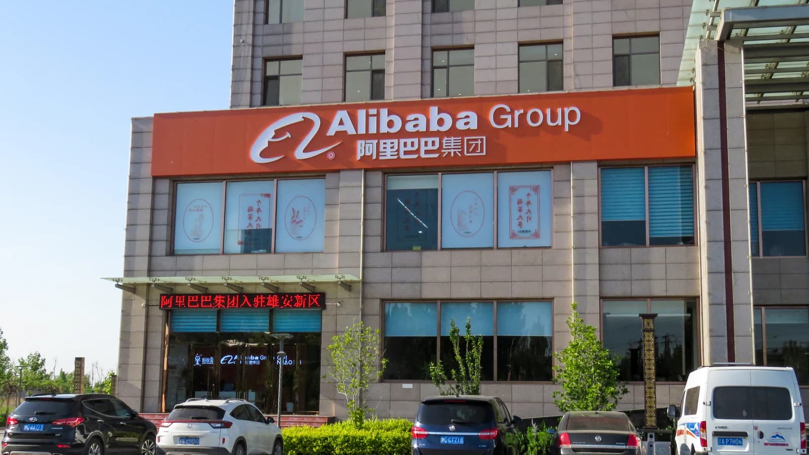 Фасад офисного здания с крупной вывеской Alibaba Group и припаркованными автомобилями